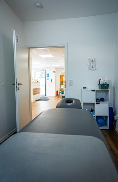 Blick auf einen Behandlungsraum mit einem Behandlungstisch und offener Tür zum Flur.