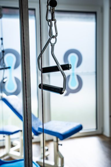 Fitnessgerät mit Griffen, im Hintergrund eine Fensterfront mit verschwommenem Muster.