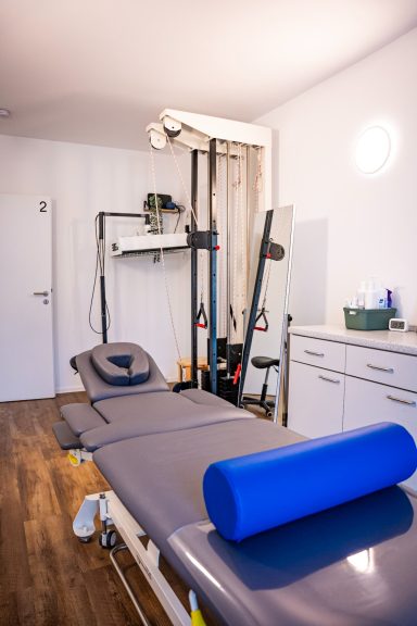 Behandlungsraum mit Therapieliege, Trainingsgeräten und blauer Rolle.