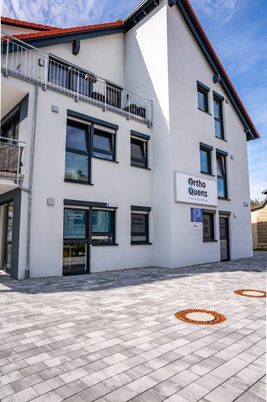 Modernes Gebäude mit großer Fassade und klaren Fenstern in einem gepflasterten Bereich.